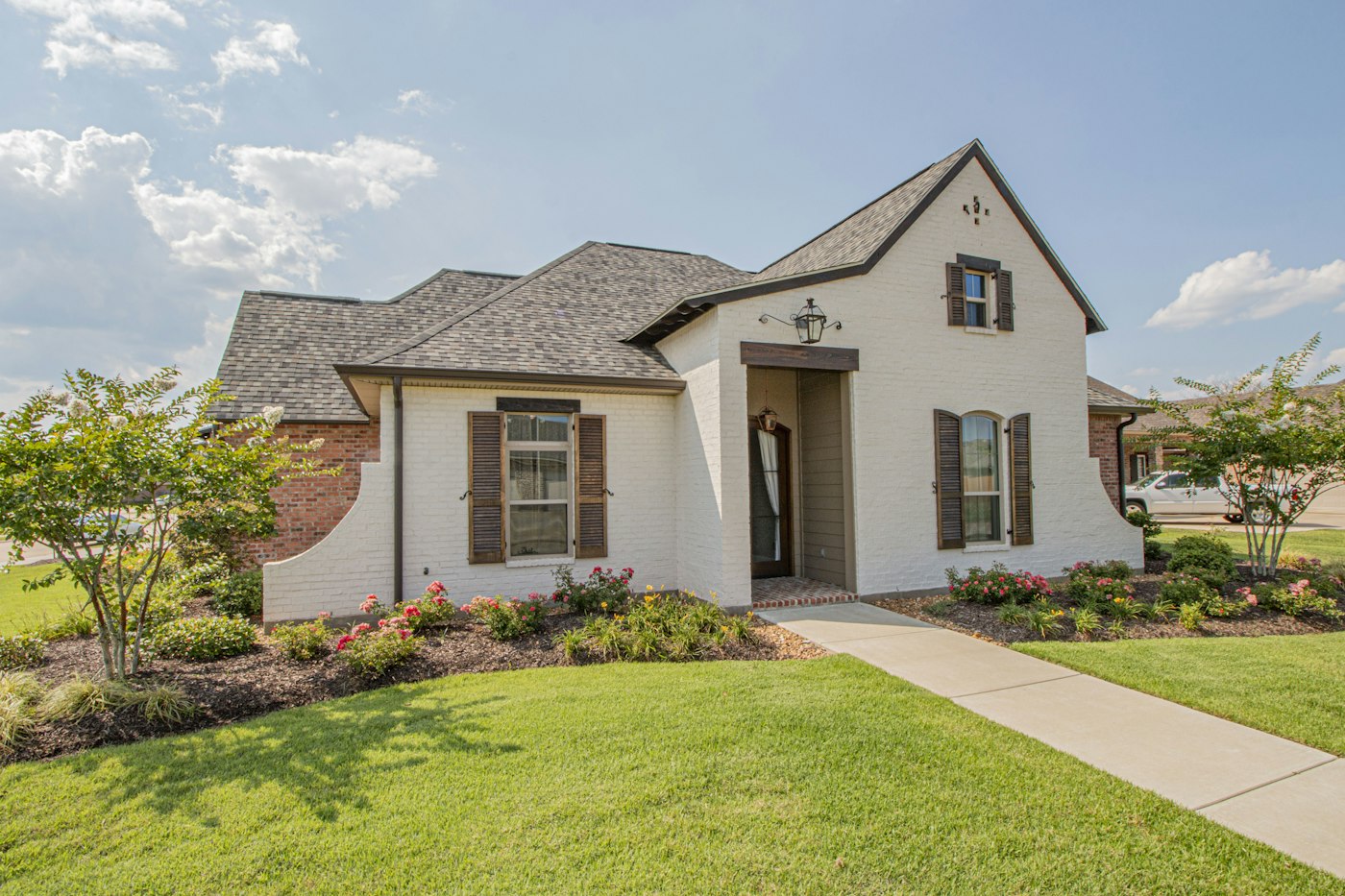 White brick house with a dark grey roof, brown shutters, and a path across the lawn.